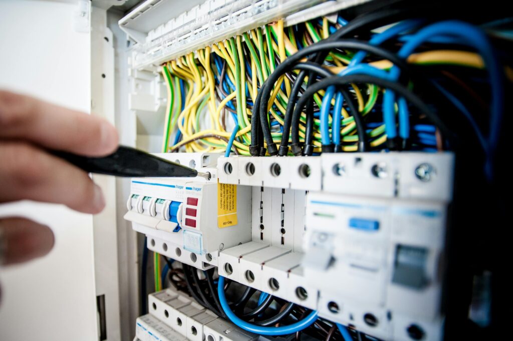 Sawh Maintenance Electrician Hand of electrician working on a circuit breaker panel with colorful wires, ensuring safe electrical connections.